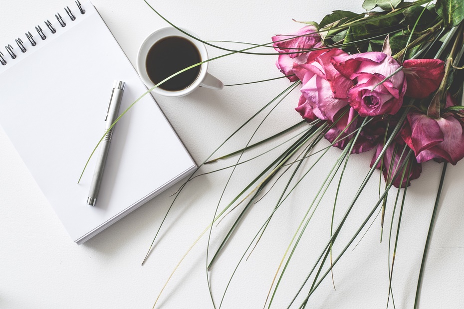 Notizblock mit Stift neben Kaffetasse und Blumenstrauß